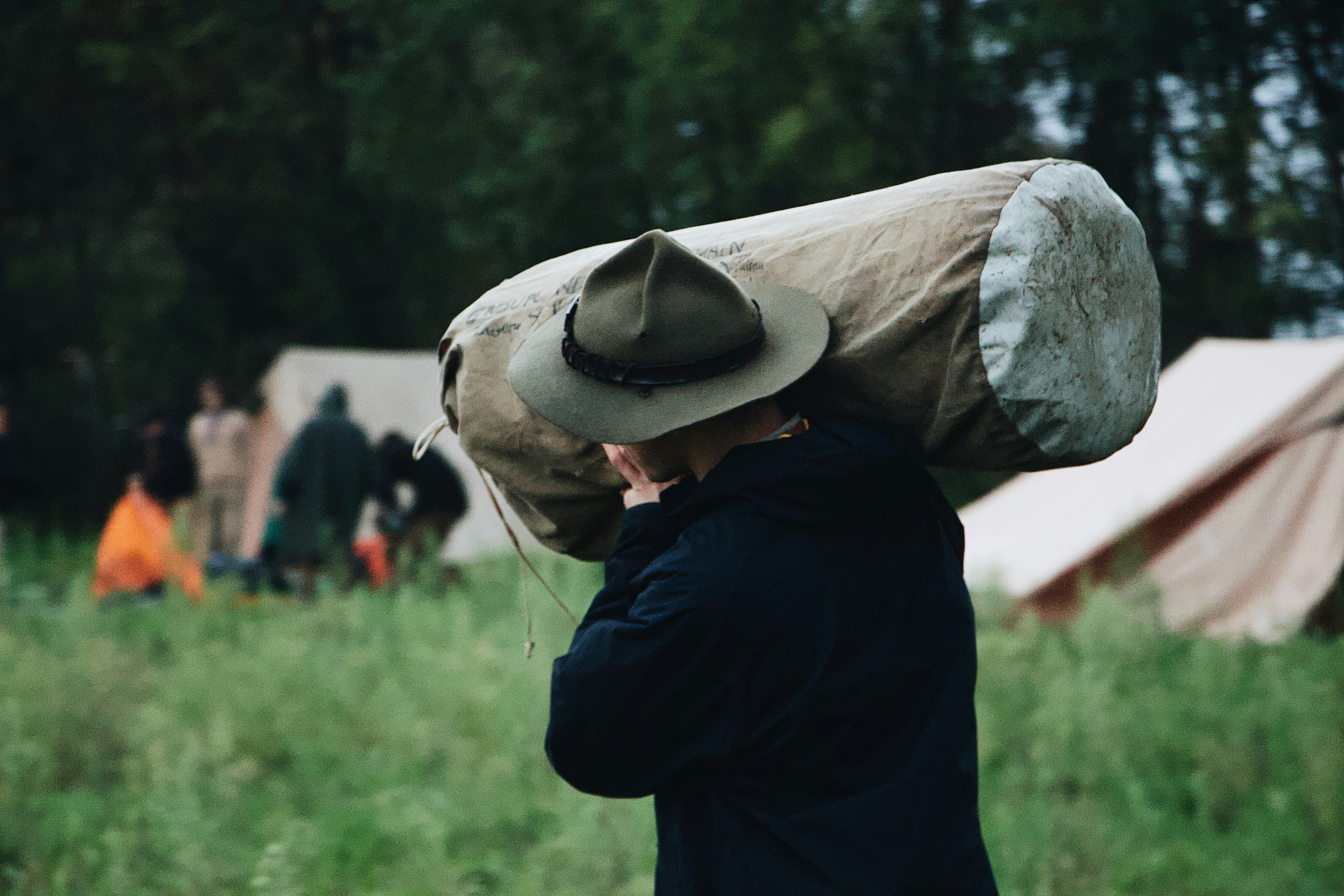 selective focus photography of walking man carrying bag near set-up tent